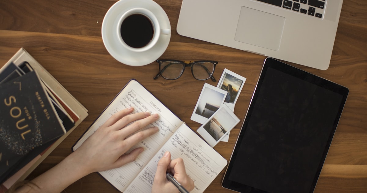 Student studying with notebook, laptop, and tablet on a wooden desk